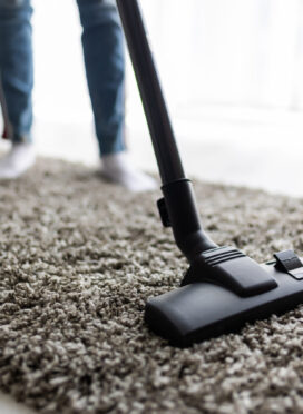 Close up of woman with legs vacuum cleaner cleaning carpet at home