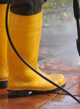 A person wearing yellow rubber boots with high-pressure water nozzle cleaning the dirt in the tiles